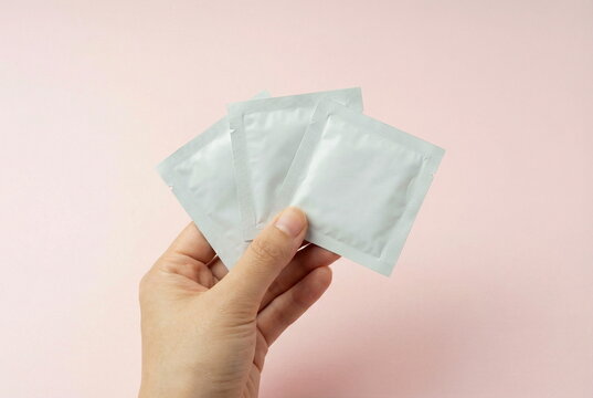 Hand holding three small white facial mask , sashet set, cosmetic products packaging blank mockup on pale pink background. Product presentation. Space for text and logo