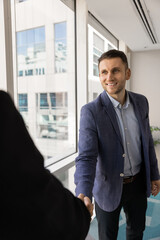Fototapeta premium Businessman shaking hands colleague stands un modern workspace. Sales manager, financial advisor or executive greeting client, starting or finalizing formal meeting in company office. Deal, etiquette