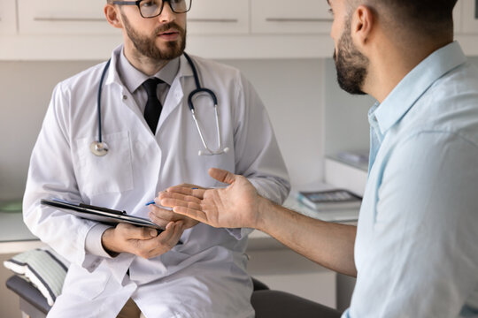 Active listening for correct diagnosis. Cropped close up focused male doctor sit on medical couch hold clipboard pen interview patient discuss concerns complaints take notes of symptoms in paper chart