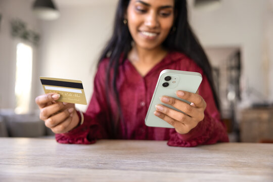 Positive young Indian consumer woman paying for purchases by credit card, using mobile phone for shopping on e-commerce platform, managing account on bank financial application. Cropped close up shot
