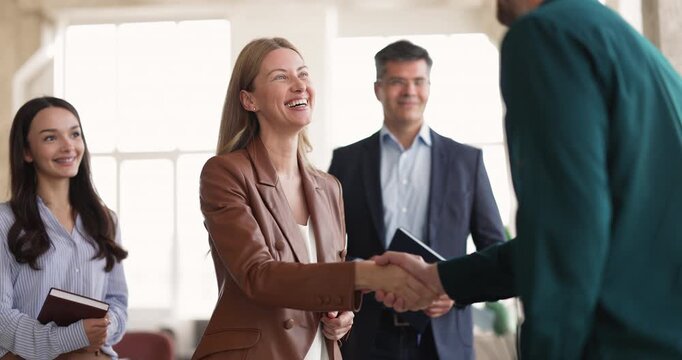 Happy businesswoman greeting male client during group meeting in office, handshaking, closing successful deal, approving partnership. Business relationship building, consulting services, agreement
