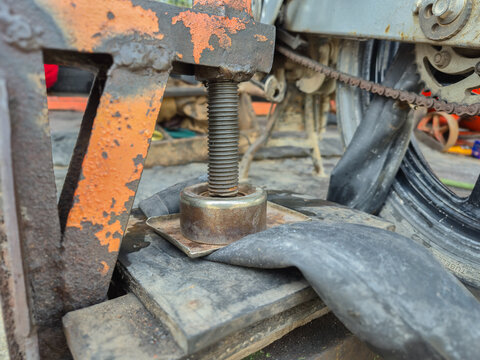 Manual vulcanizing press machine patching a motorcycle inner tube at a traditional roadside repair shop. Old mechanical tool for fixing flat tires in a workshop