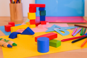 Brightly colored wooden building blocks, crayons, and paper cutouts arranged on a table,...