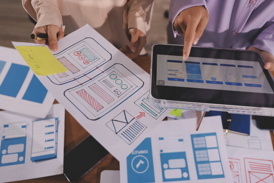 Close up ux developer and ui designer brainstorming about mobile app interface wireframe design on table with customer breif and color code at modern office.Creative digital development agency.