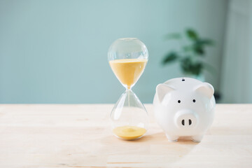 Fototapeta na wymiar Save money and invest dividend income interest fund in pig piggy bank, hourglass with yellow sand on wooden table shows time management and productivity for long term financial goals
