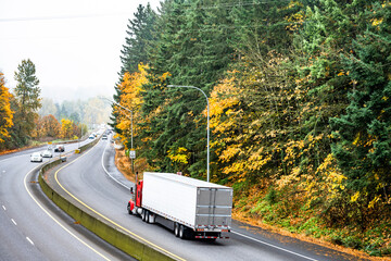 Red bonnet big rig semi truck transporting cargo in refrigerator semi trailer running on the autumn...