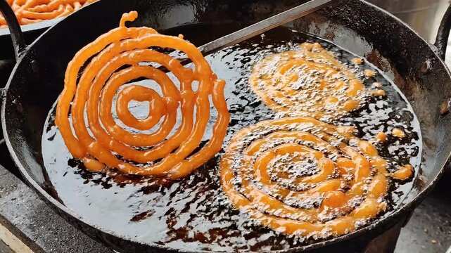 Crispy orange jalebi frying in hot oil in a large black iron pan during the preparation of traditional sweet dessert in a local market