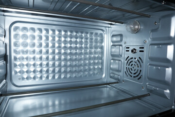 Interior view of a clean, empty electric oven with metal heating elements, textured back panel, and...