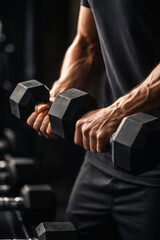 Naklejka na ściany i meble Close-up of a muscular man's arms performing bicep curls with dumbbells in a gym setting.