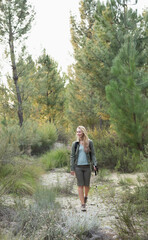 Naklejka premium Adult woman hiking sandy trail in pine forest, holding pole, wearing hiking boots and backpack