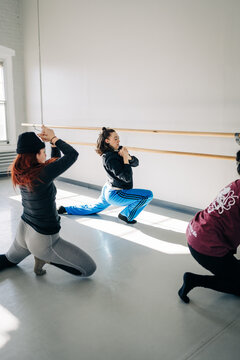 Dancers in lunge pose during rehearsal beside studio barre
