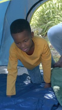 Vertical video: Kid in shirt crawling, testing pad and sitting in tent as adult adjusting green bag