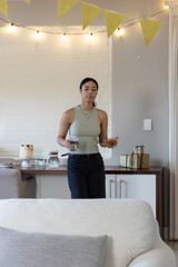 Obraz premium African american woman holding glass of water in living room with frosted cake, string lights