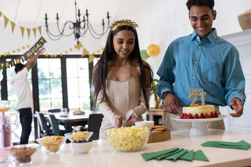 Diverse friends preparing green napkins, snacks, strawberry birthday cake on kitchen island