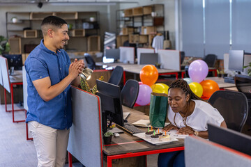 Diverse coworkers celebrating birthday at office with cupcakes, balloons, gift bag, copy space