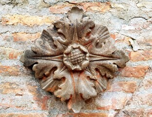 
A stone flower with leaves is on a wall. The flower is brown and has a leafy design
