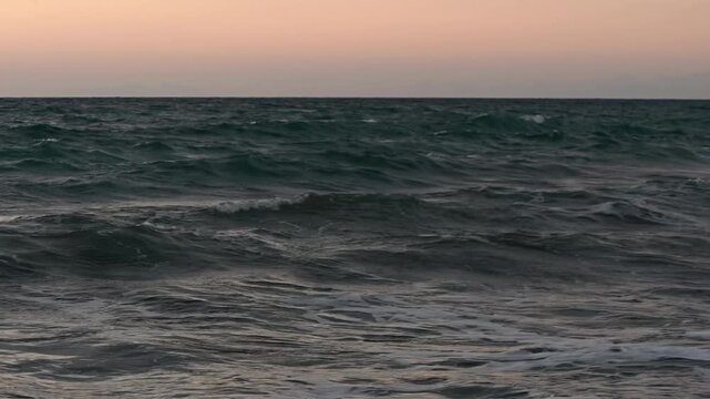 Breathtaking wide cinematographic shot of the sun setting behind the Mediterranean Sea horizon, casting brilliant orange, pink and golden light across the water. Silhouettes of rugged Cyprus coastline