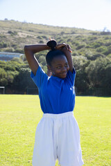 Naklejka premium African american girl stretching arms above head on soccer pitch near goal frame wearing shirt