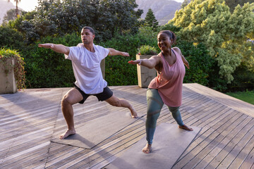 Obraz premium Diverse couple practicing yoga in sportswear on open-air deck with yoga mats, potted plants