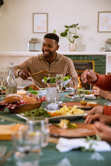 Naklejka premium African american man serving salad from large bowl with spoon at dining room table