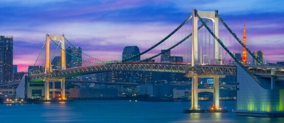 Naklejka premium Tokyo Rainbow Bridge Illuminated at Night with City Skyline and Bay Reflections Panorama