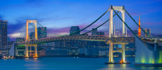 Naklejka premium Tokyo Rainbow Bridge Illuminated at Night with City Skyline and Bay Reflections Panorama