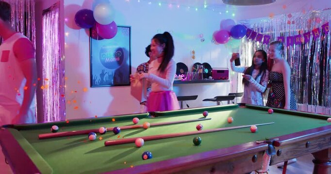 Guests gathering around birthday pool table, woman offering man gift and sparking selfie posing