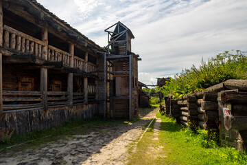 The impressive wooden walls of a reconstructed Old Slavic fortress, made of round, hewn logs. Old barracks and boyar chambers. A bright, sunny day.
