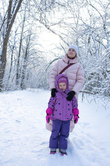 Fototapeta premium Cheerful family mother and little daughter spending time together in snowy park on winter weekend