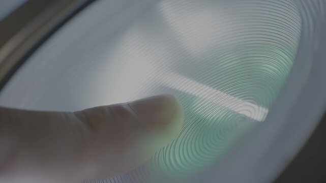 Close-up of a finger pressing on a smooth, illuminated surface with concentric patterns, showcasing the interaction with light and texture in a modern setting, hdr video with neutral color