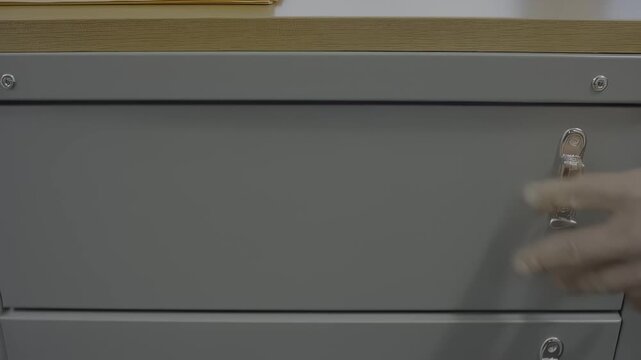 Close-up view of a hand wearing a glove reaching into a filing cabinet drawer filled with organized documents,  process of retrieving important files in an office setting, hdr video with neutral color