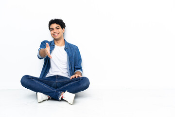 Venezuelan man sitting on the floor shaking hands for closing a good deal
