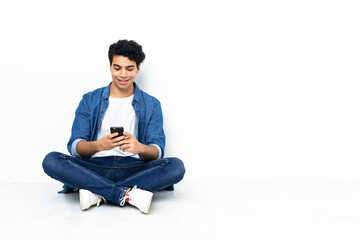 Venezuelan man sitting on the floor sending a message with the mobile