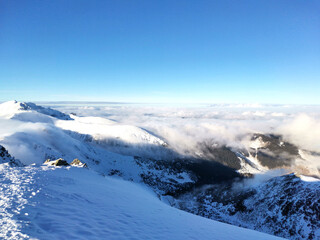 Snow capped mountain peak surrounded by clouds. View from above. Clear sunny winter day. Above the clouds.