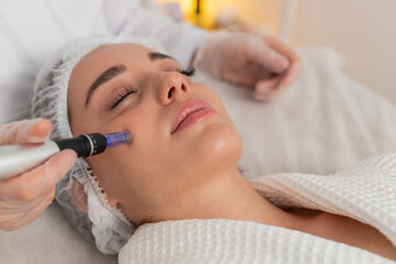 Fototapeta premium Peeling, woman health care, skin regeneration, dermapen microneedling, dermastamp. Beautician cosmetologist doing forehead face procedure fractional microneedle mesotherapy clinic facial rejuvenation