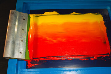 An artisan applies layers of warm colored inks on a screen, blending fiery hues to produce a smooth gradient. The image showcases the creativity and tactile approach of traditional hand printing © Narong Niemhom