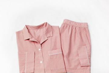 Top view of folded red striped pajama set on white bed. Minimal style, cozy, comfort pyjamas. Pink...