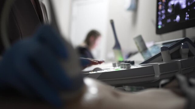 Healthcare workers administering gel and utilizing a transducer on a patient's abdomen during an ultrasound procedure, with a second doctor operating the ultrasound machine in the background