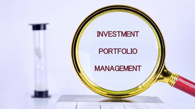 A magnifying glass reveals scattered red text forming Investment Portfolio Management. An hourglass rests on a white desktop, symbolizing careful financial timing and strategic planning