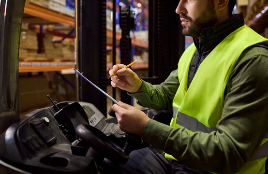Forklift operator checks clipboard for warehouse inventory. Close view of a warehouse worker recording inventory on a forklift before loading. Warehouse logistics enabling delivery storage.