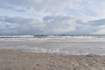 Dramatic stormy sky over an empty sandy beach with waves and dark clouds. Moody seascape landscape with strong wind, cold atmosphere and vast open space. Minimalist coastal scenery, solitude and natur