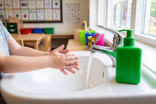 Child washing hands in classroom sink with soap and green dispenser