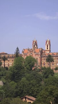 Panoramic view of the historic Comillas Pontifical University building, a masterpiece of modernist architecture, sitting atop a green hill under a clear blue sky on a sunny day in Spain
