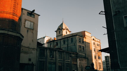 Obraz premium A building stands tall, framed by adjacent structures. Sunlight illuminates the facade, creating shadows. Architectural details are visible. The sky appears overcast