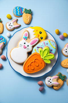 Easter holiday background with easter cookies in a plate: bunny, chick, carrot and egg on blue background, with mini chocolate egg candies