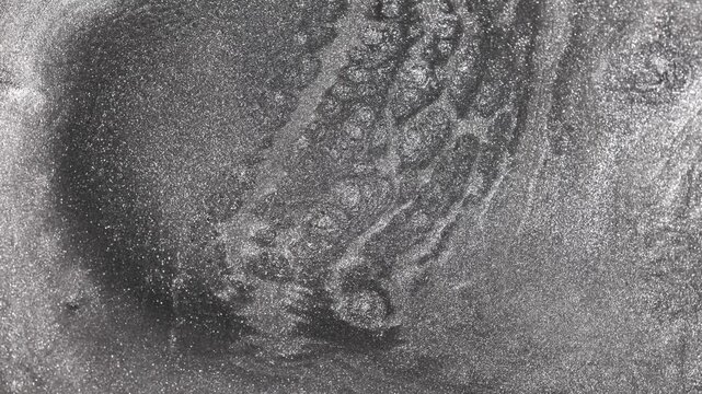 Detailed close-up of fluid silver paint swirling and settling slowly revealing intricate sandy texture and shimmering titanium particles forming complex webbed patterns on abstract grey background