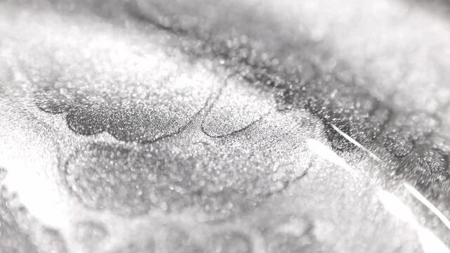 Macro shot of silver platinum paint with specialized sandy texture flowing slowly into heavy waves and ridges while sparkling radiant glitter particles shift in light and reveal deep contrast on 