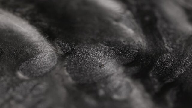 Dark titanium paint flowing heavily with a sandy texture forming deep undulating ridges and showcasing glittering metallic particles on the surface