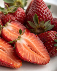 A fresh organic strawberry and juicy slices on a white plate are isolated for a healthy summer dessert featuring macro details of ripe red fruit