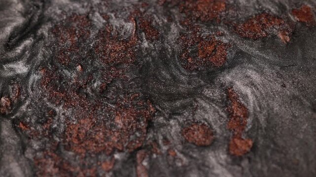 Macro shot of dark graphite fluid swirling and churning with rust-colored copper glitter particles to form intricate metallic patterns on dark background